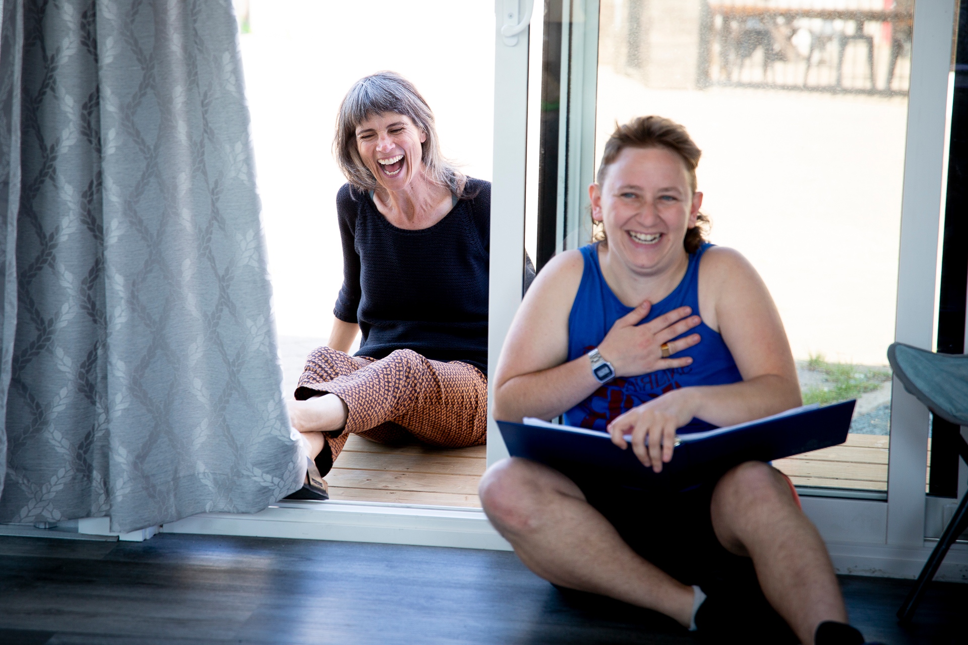 Two white actors, one beautiful woman, one beautiful non binary person sit side by side and laugh joyfully. It is all happiness.